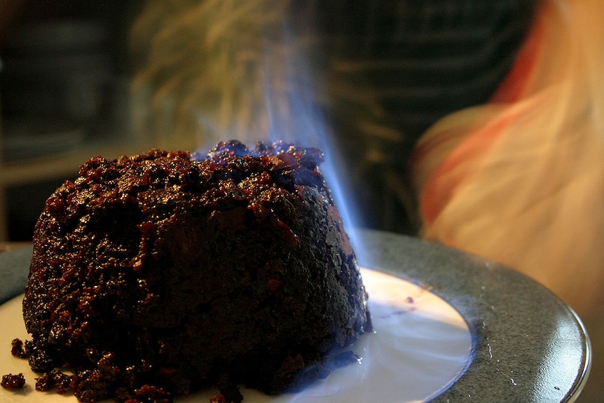 Plum pudding on a plate, with a slight blue flame (flambe) on the pudding.