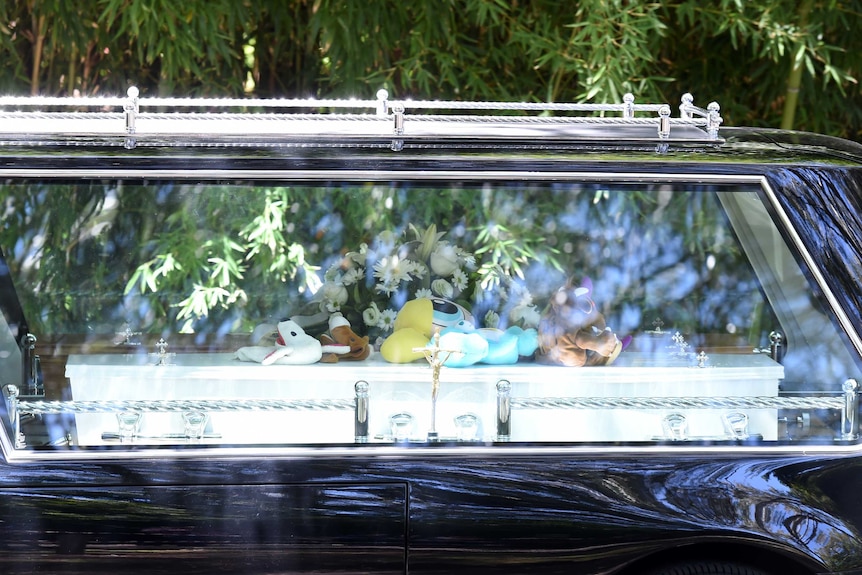 A hearse carrying a coffin with toys on top of it departs the Lutz-Manrique family funeral.