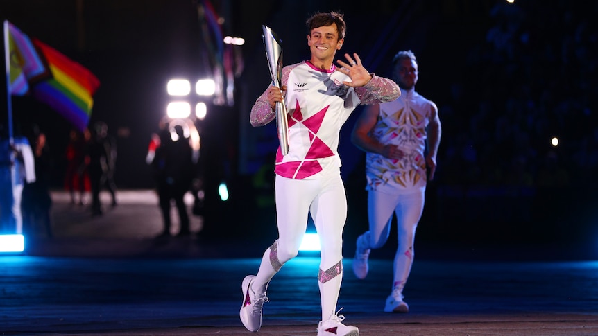 British diver Tom Daley jogs and waves while carrying the baton at opening ceremony for the Birmingham Commonwealth Games.