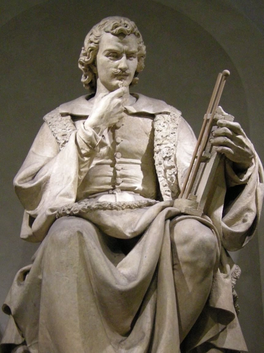 A white, marble statue of an Italian man holding an early barometer.