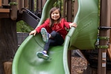 A young girl sits at the top of a slide on a playground 