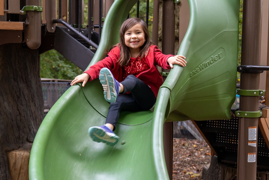 A young girl sits on top of a slide on a playground 