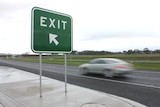 A car drives past a freeway exit sign.