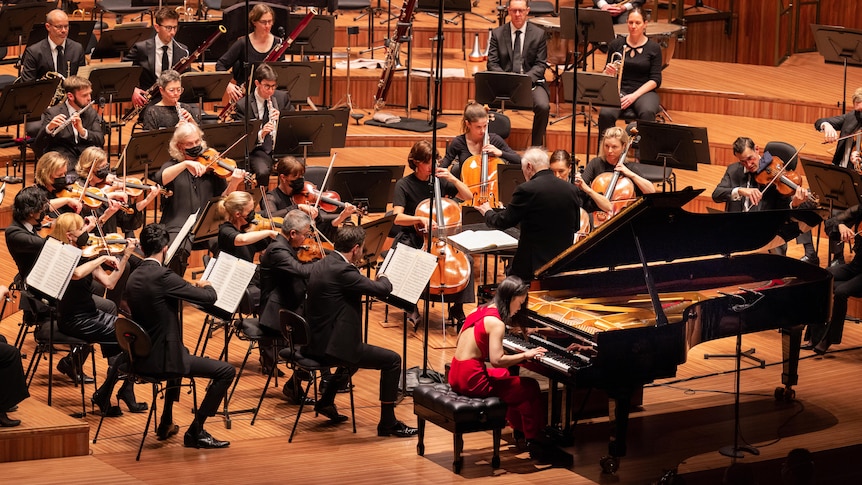 Korean pianist Yeol Eum Son in a red dress playing onstage with the Sydney Symphony Orchestra.