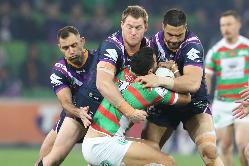 Alex Johnston is tackled by three Melbourne Storm players.