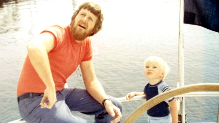 A man with a beard sits on a yacht next to a young blonde haired boy in the 1970s