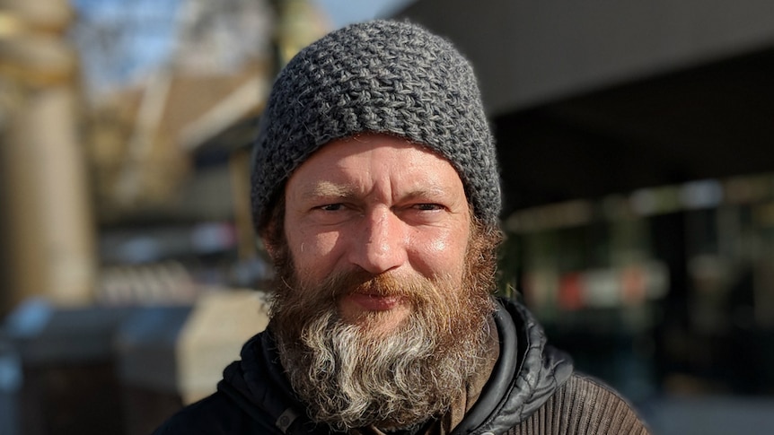 A man with a beanie and long beard, standing out on the street
