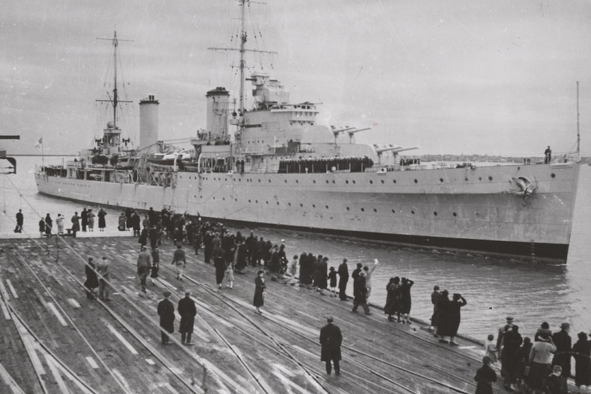 A black and white photo of a naval ship berthing at a Melbourne pier with people waiting on the dock