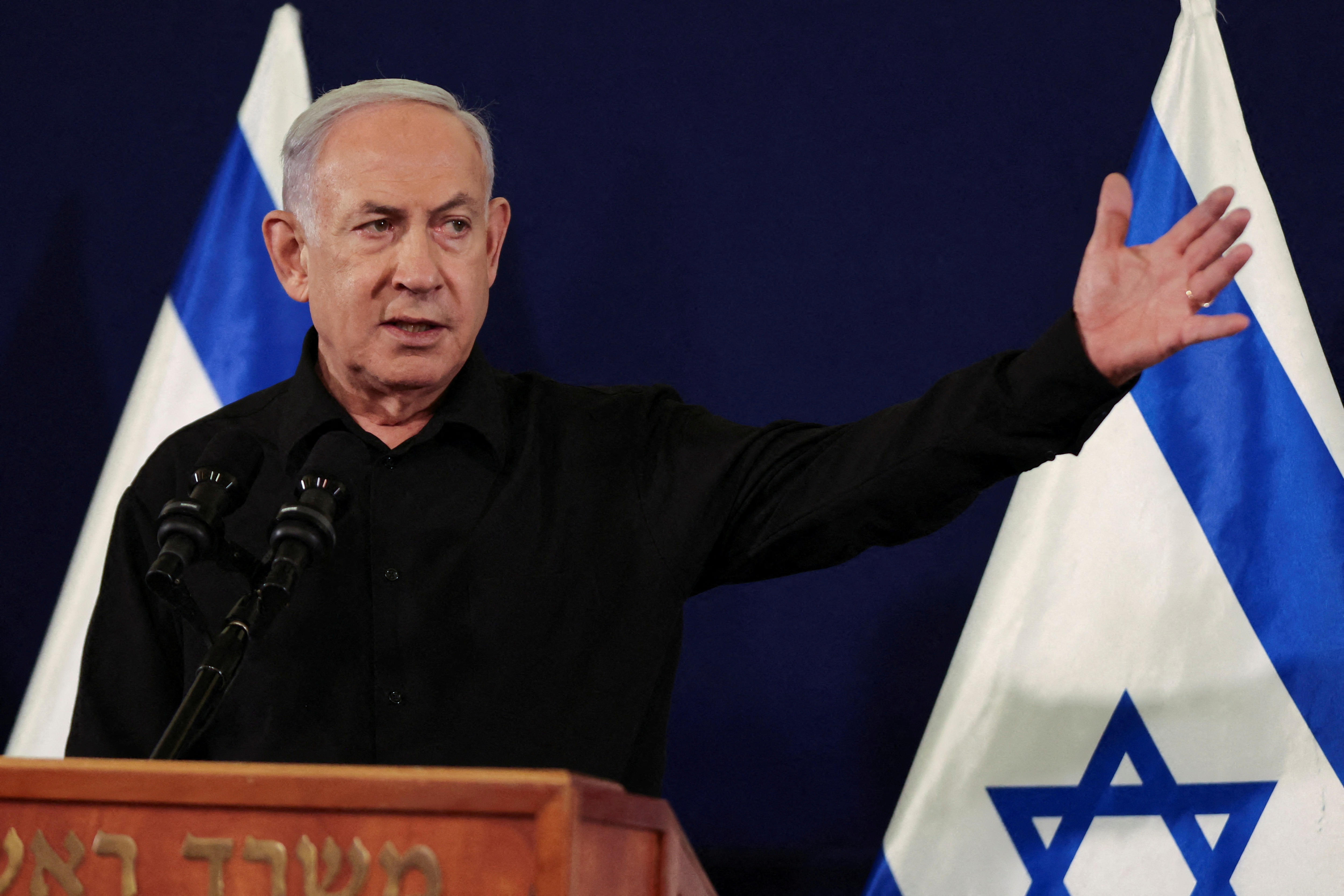 Benjamin Netanyahu gesticulates at a media conference with the Israel flag behind him