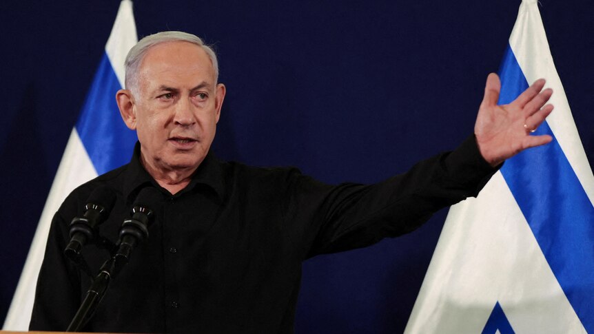 Benjamin Netanyahu gesticulates at a media conference with the Israel flag behind him