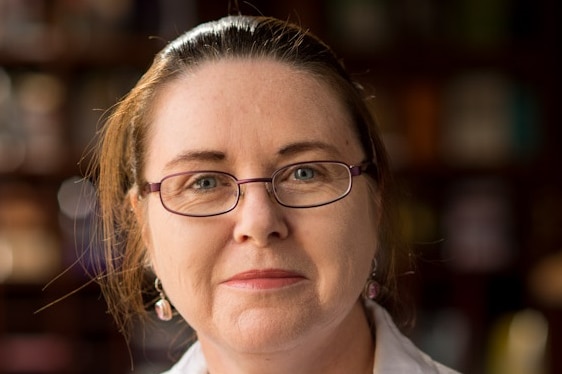 A woman wearing glasses looks into the camera.