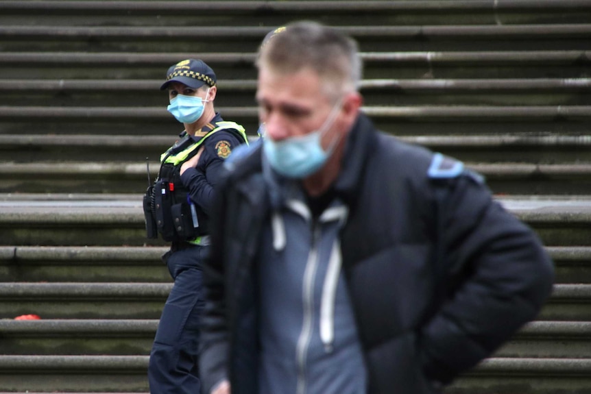 A mask-wearing police officer seen over the shoulder of a man wearing a mask.