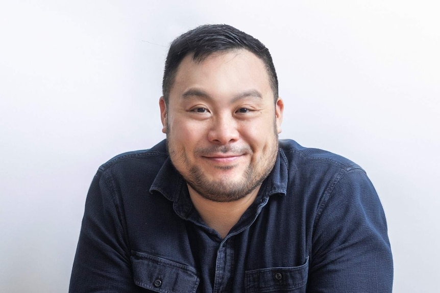The chef David Chang wearing a blue shirt sitting at a bare table