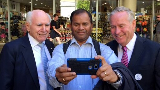 A man holds a camera out to take a selfie of himself flanked by John Howard and Colin Barnett.