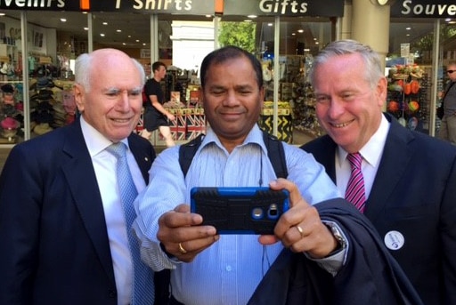 A man holds a camera out to take a selfie of himself flanked by John Howard and Colin Barnett.