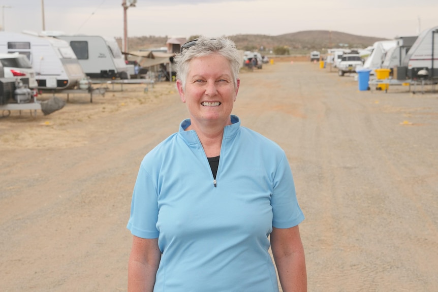 A grey-haired woman in a light blue short smiles.