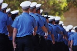 Police recruits march in uniform with their backs turned in a graduation ceremony.