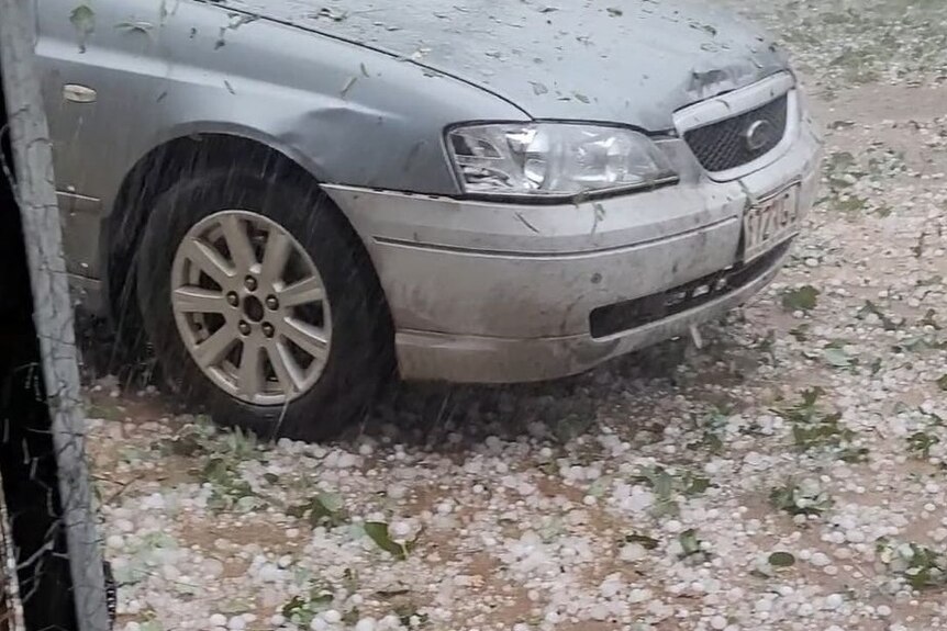 Large hail at the base of a silver Ford, leaves strewn around too.
