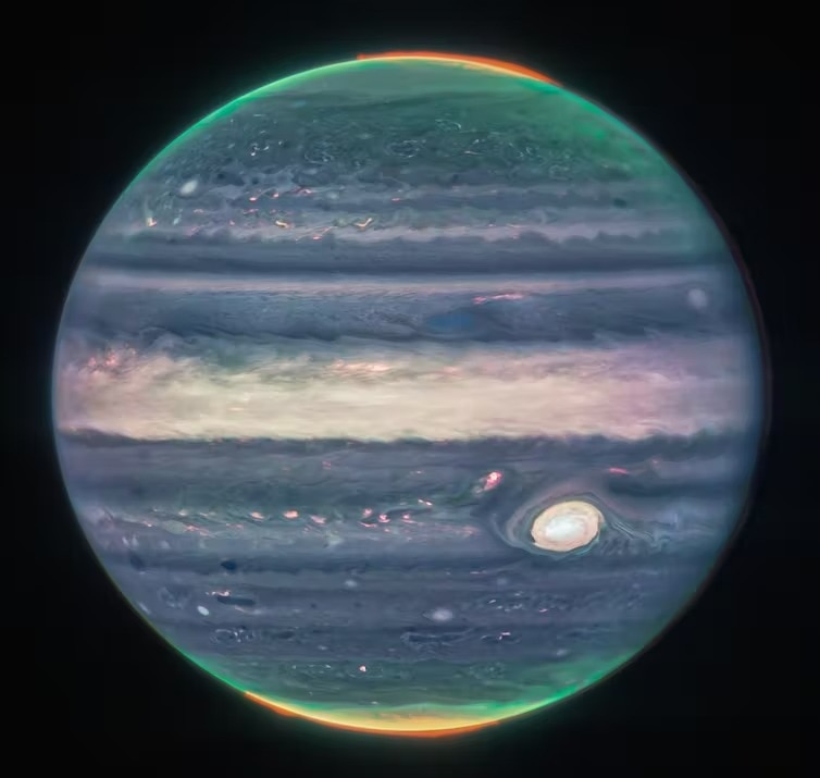 a photo of jupiter with a blue tinge, with multi-colour glow at each pole