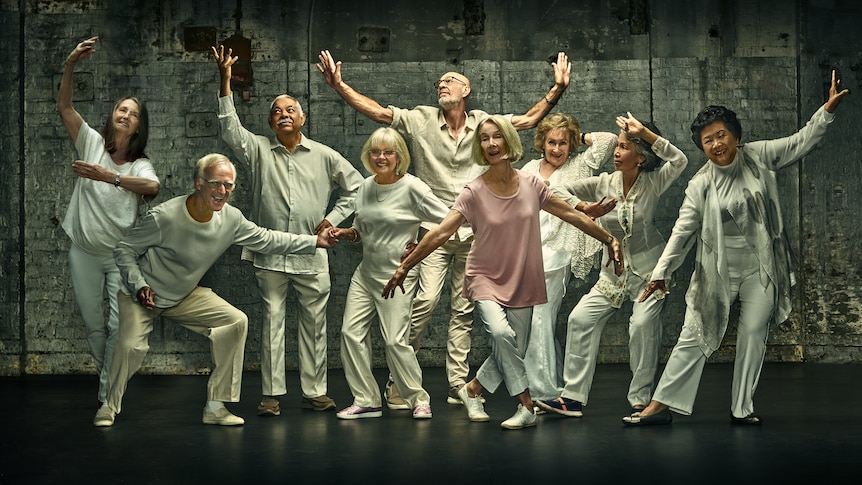 A group of nine older people wearing white in various dance poses