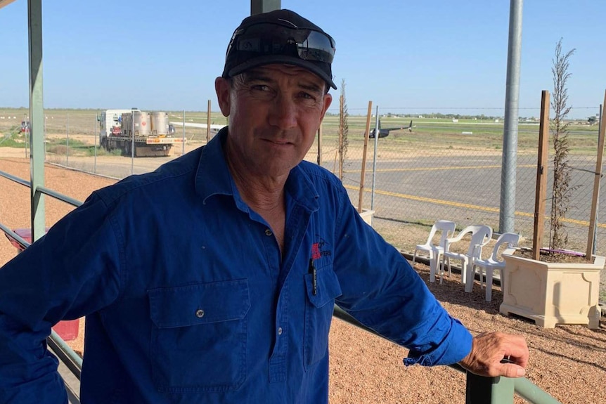 A man looks at the camera while a helicopter sits on the tarmac in the background.