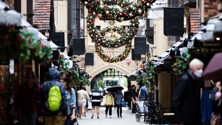 Large Christmas wreathes hang over a street filled with boutique stores, and people.
