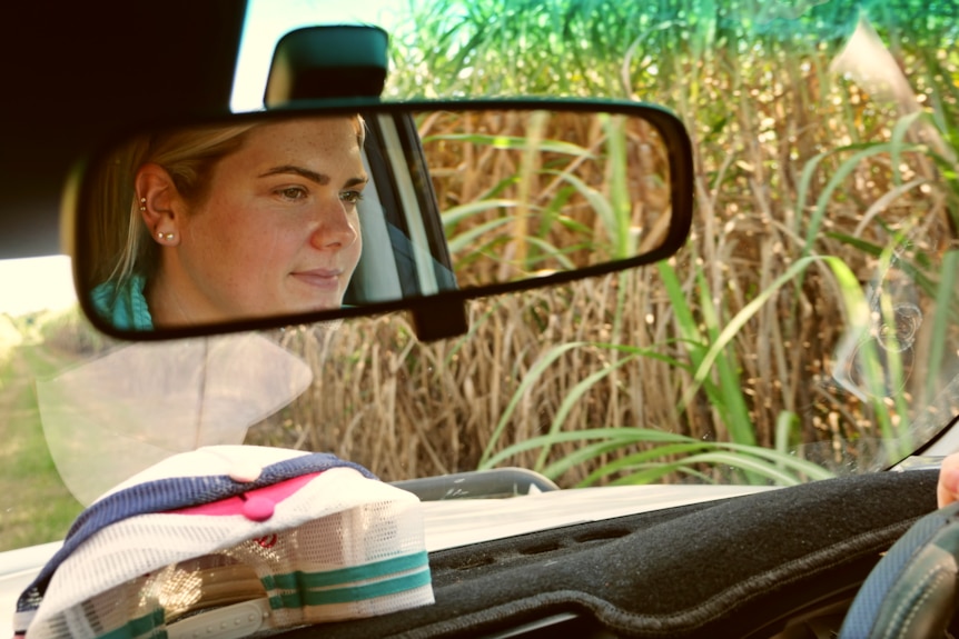 a woman driving the car is visible in the rearview mirror surrounded by cane
