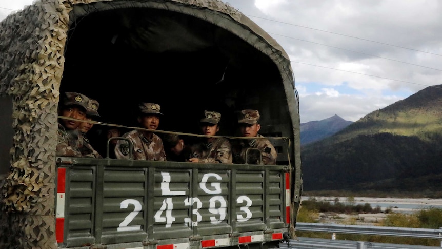 Soldiers in back of army truck driving through mountainous region.