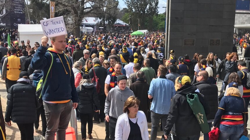 A man holds a sign outside the MCG looking for tickets on grand final day.