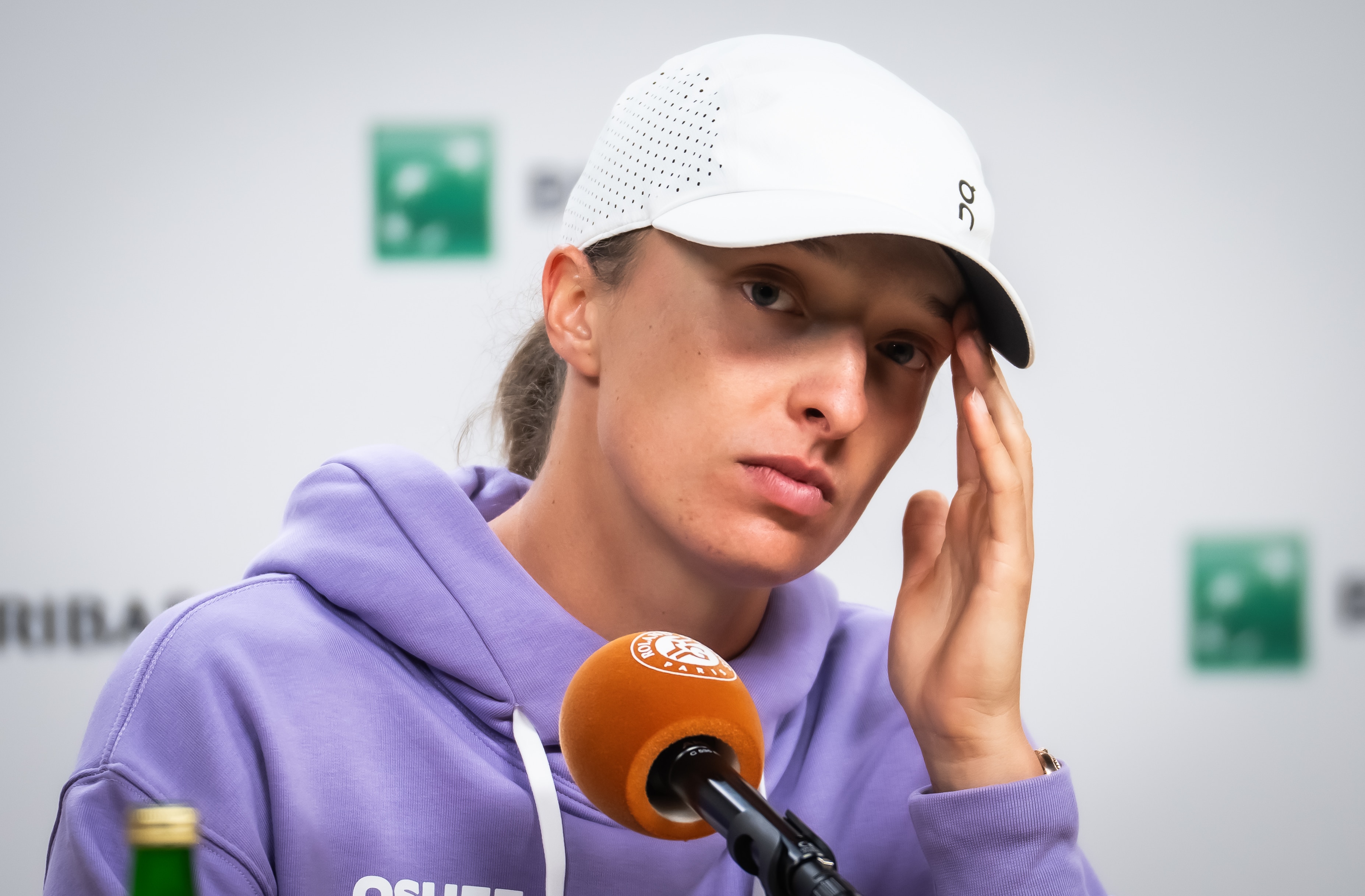 Iga Swiatek touches her head while looking glum in a French Open press conference.