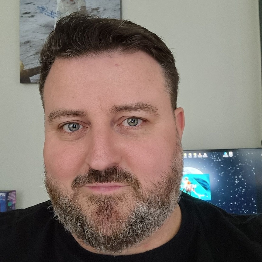 A portrait selfie of a man with brown hair and a beard wearing a black tshirt.