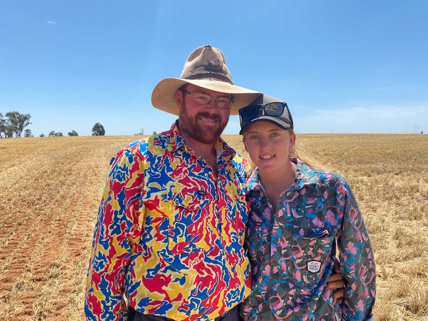 A man and his daughter standing in a barley crop with blue sky behind they are smiling.