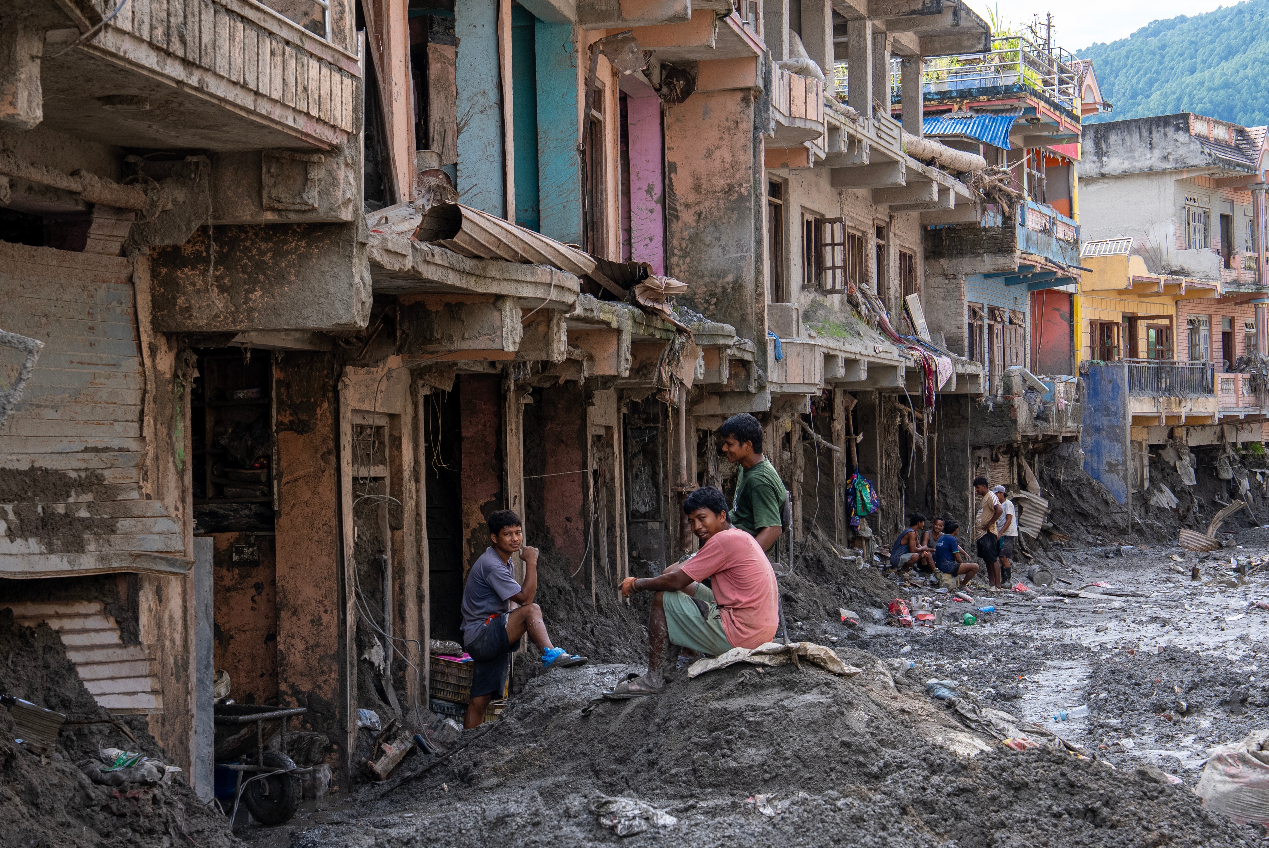 In a ravaged city street, covered in mud and debris, three young men sit together and talk.