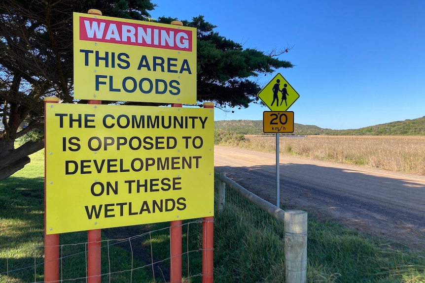 A sign says 'Warning: This area floods. The community is opposed to development on these wetlands"