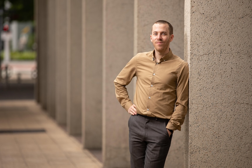 A man leans on a concrete pillar.