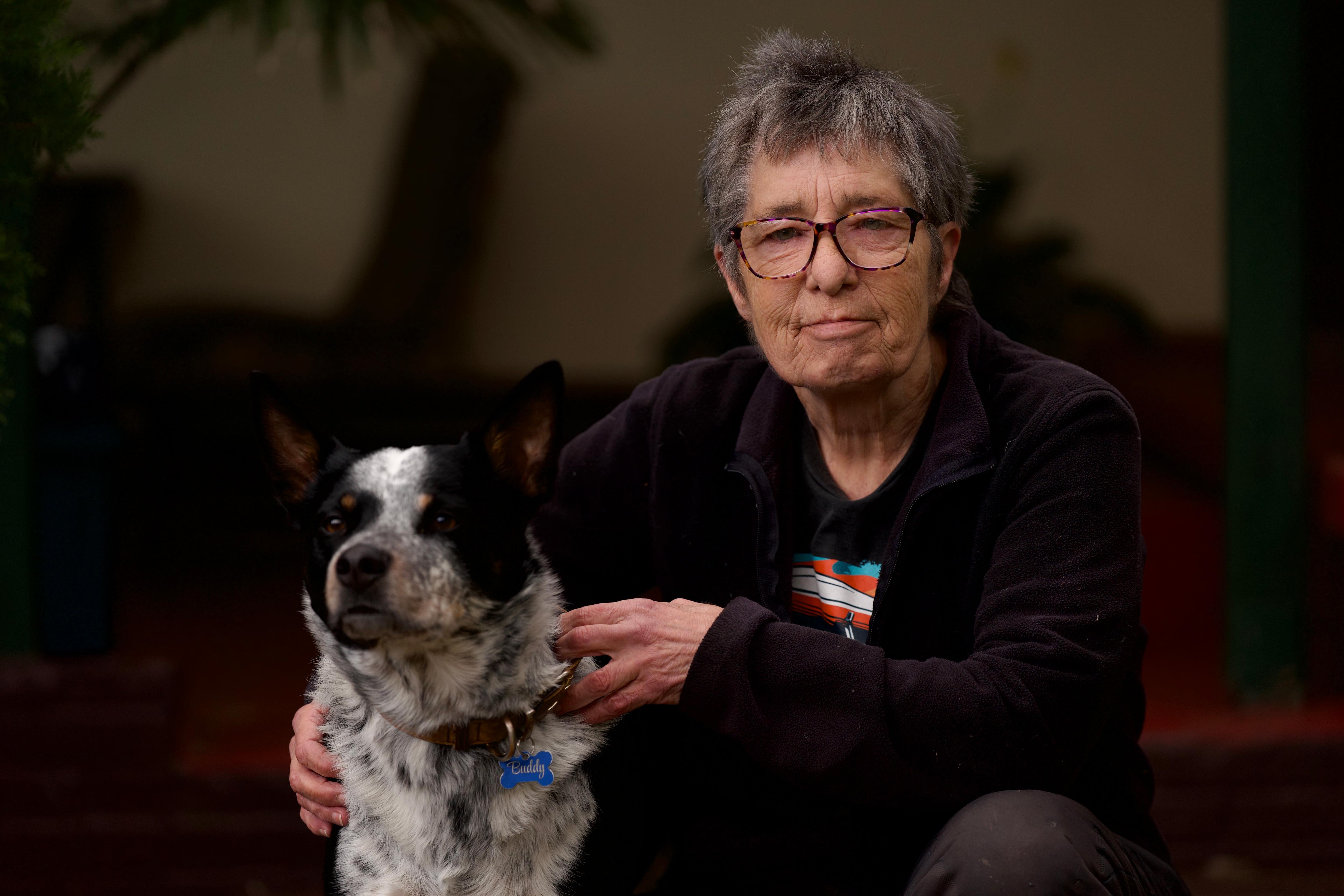 A woman kneels down next to her dog, both looking at the camera