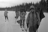 A black and white photo of four men in big jackets and skis traversing a snowy field