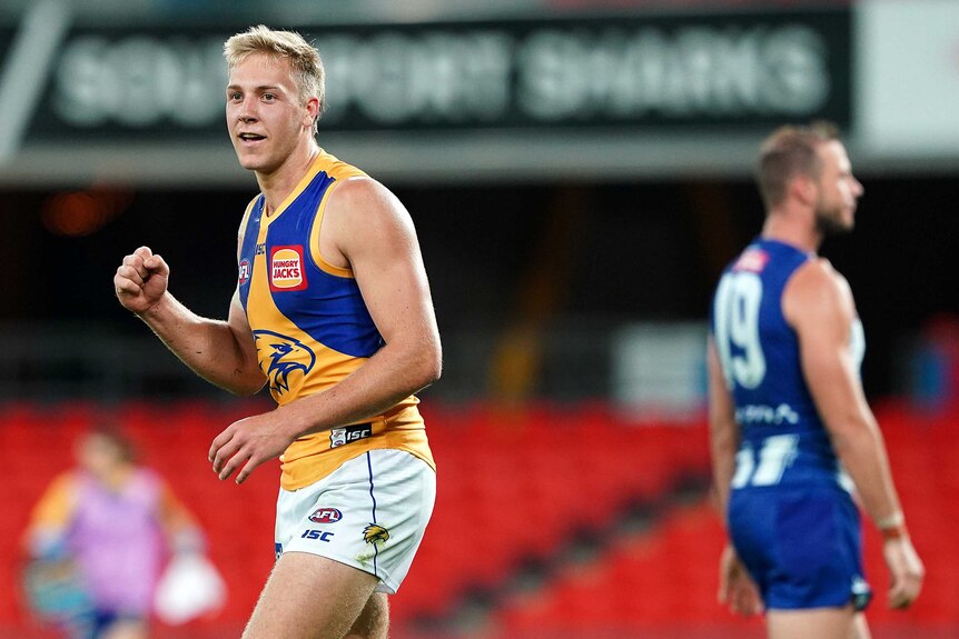 A West Coast Eagles AFL player smiles as pumps his fist while celebrating a goal against North Melbourne.