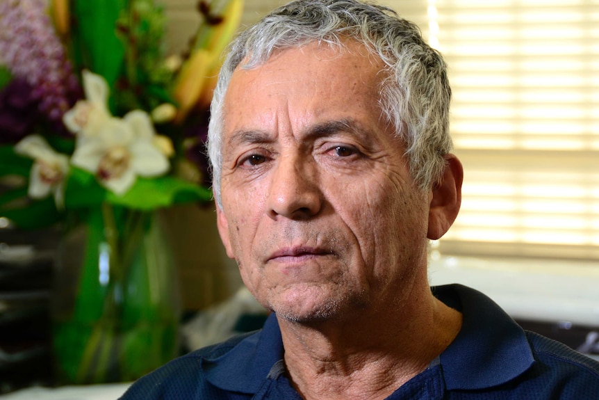 A middle aged man with grey hair wearing a blue polo shirt stairs at the camera.