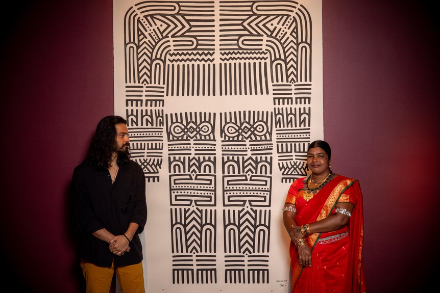 Two people standing in front of artwork detailing Baiga Tribe body tattoo.