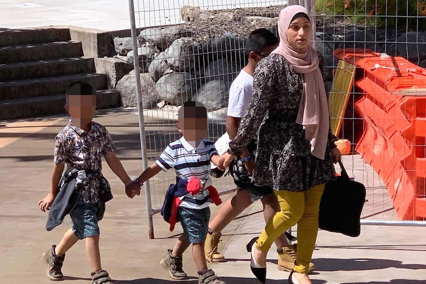 A woman and three children walking along a path in front of temporary fencing