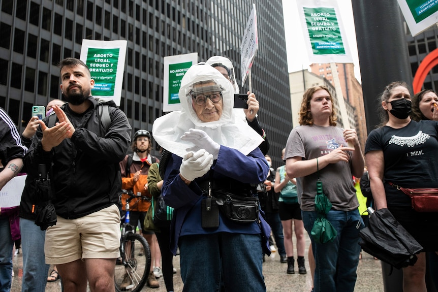 An elderly woman in a full mask claps her hands at a rally in Chicago