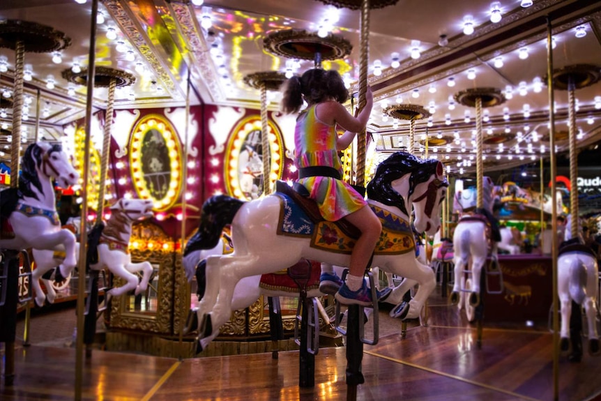 A girl with her back to the camera, clinging to a plastic horse.