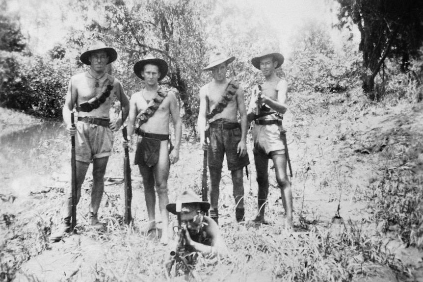 A historical black and white image of a small group of men standing in the bush, holding guns and looking serious