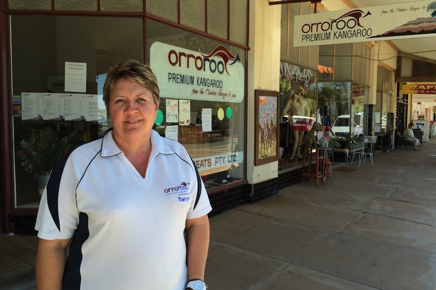 A photo of a woman standing in front of a butcher shopfront.