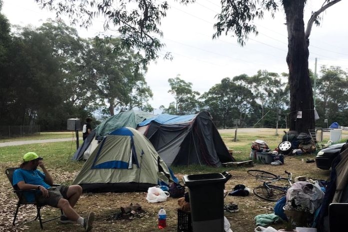A picture of someone in a camp chair with tents in the background. 