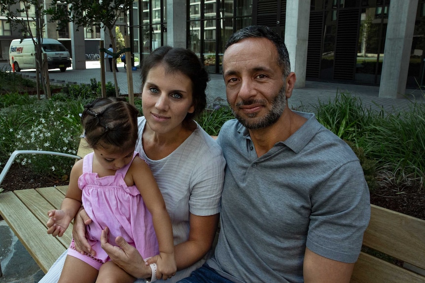 A man a woman and a young child sitting outside.