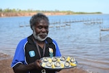 South Goulburn Island elder Bunug Galaminda holds a plate of oysters which were grown out at the farm behind him.