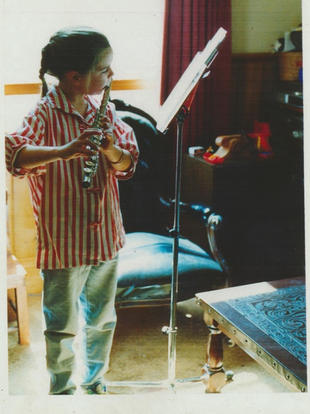 A young girl reads music on a stand and plays the flute.