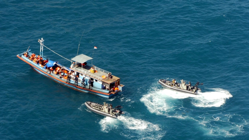 Two Border Protection Command boats surround a larger boat in the ocean.